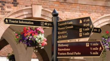 A signage post with hanging baskets of flowers behind it