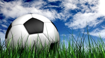 a white and black football on long green grass with a blue and white cloud sky
