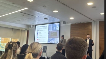 photo of people sitting in a room with a person standing upfront by a screen 