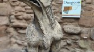 clay statue of a griffin with a castle wall behind.